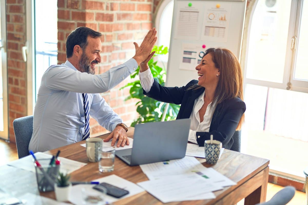 Two colleagues celebrating with a high five across a desk in a bright office