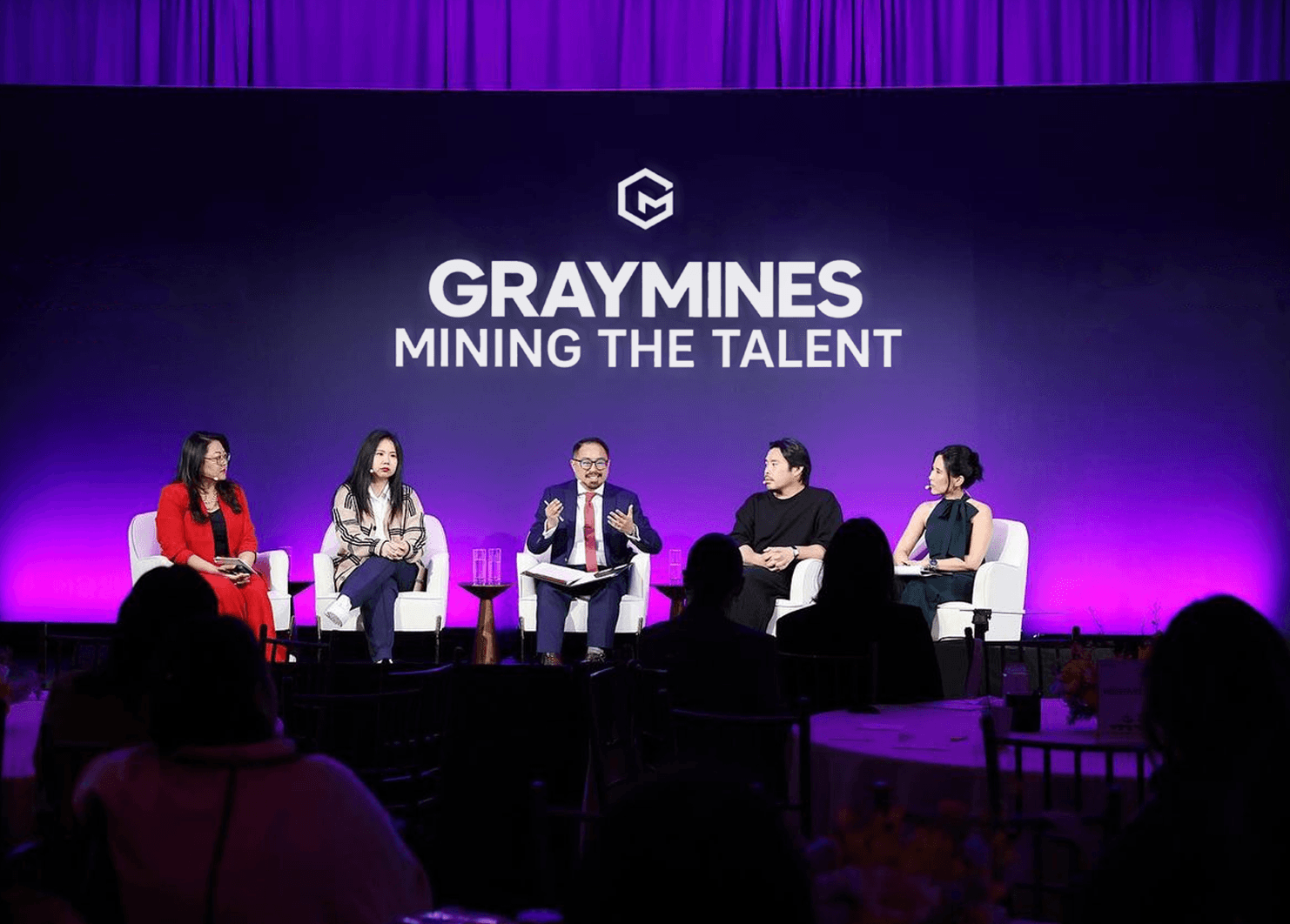 A panel of five speakers on a stage lit in purple, beneath the Gray Mines name