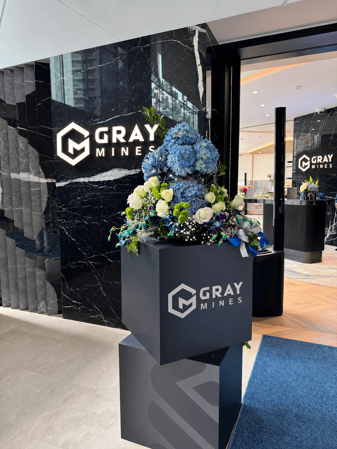 The entrance to a Gray Mines studio: the logo on black marble beside a display of flowers