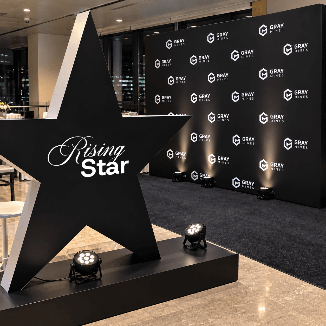 A large black star reading Rising Star in front of a Gray Mines backdrop, lit by floor lights
