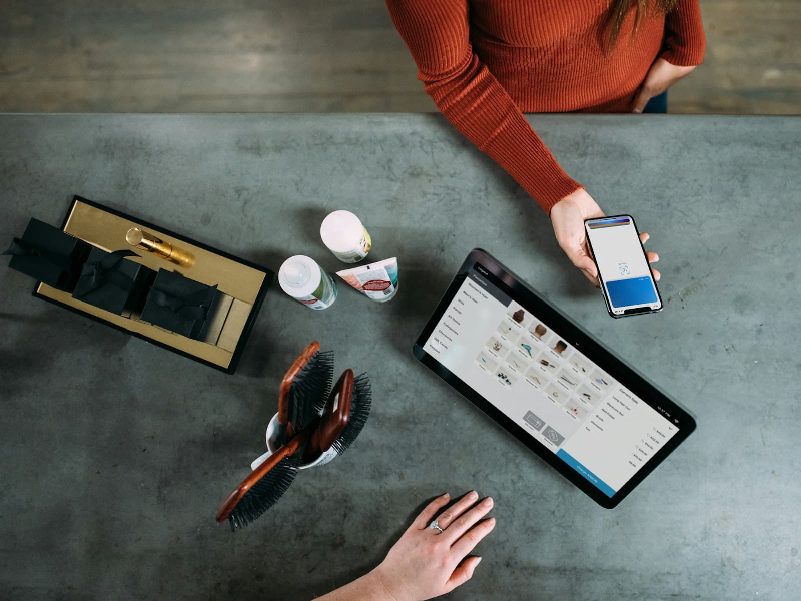 A customer paying by phone at a shop counter, beside a tablet till