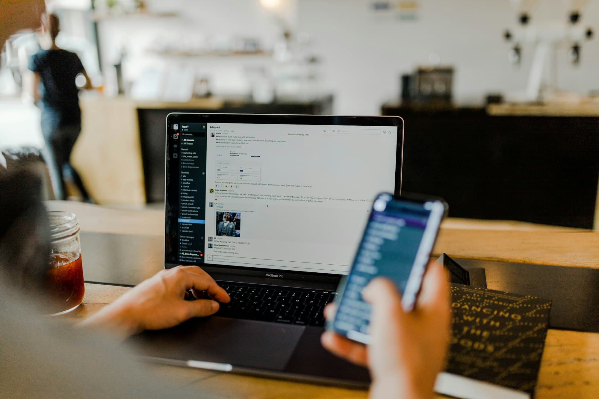 A person checking a banking app on a phone beside an open laptop