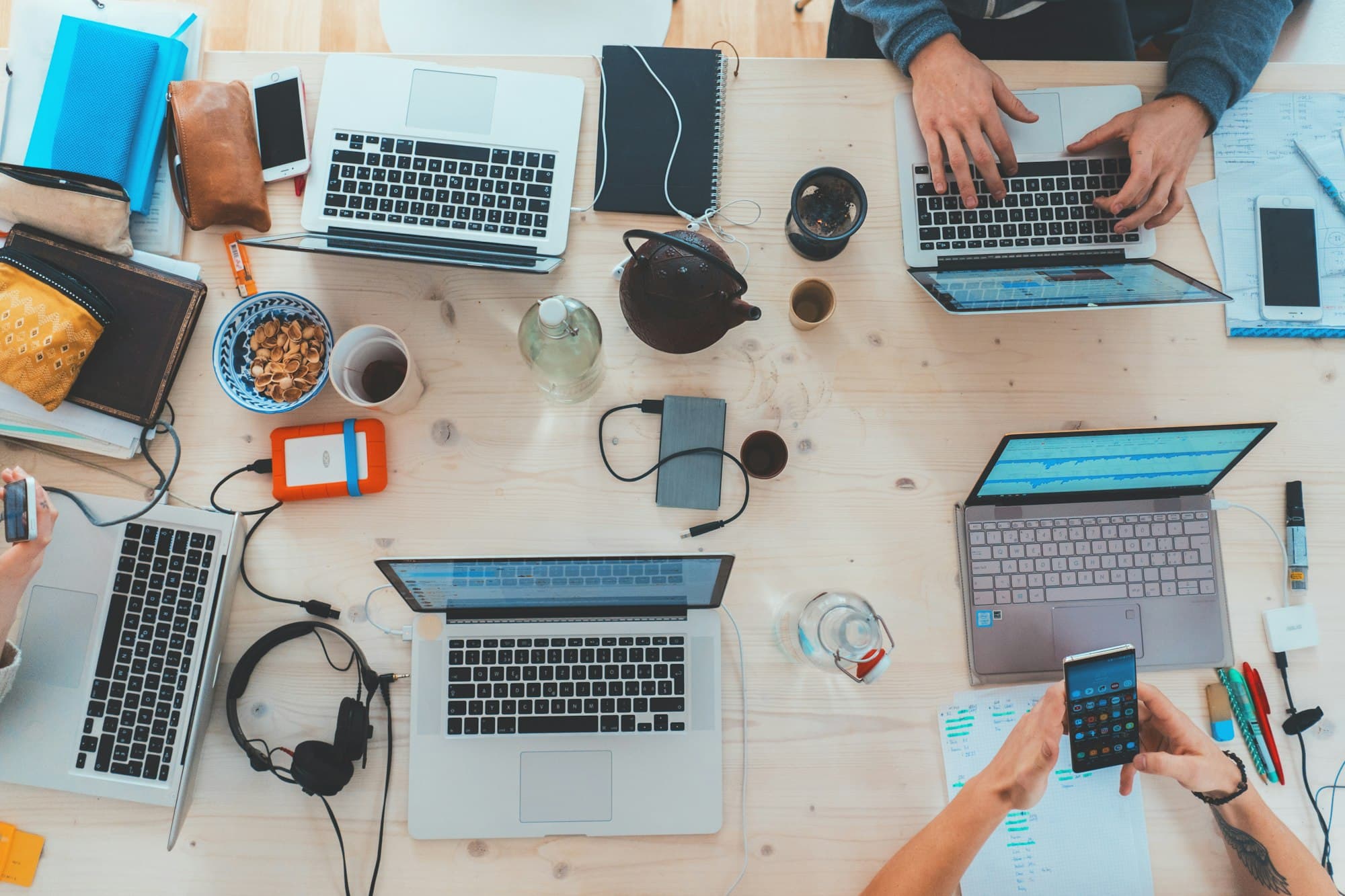 Several laptops and phones on a shared wooden desk, seen from above